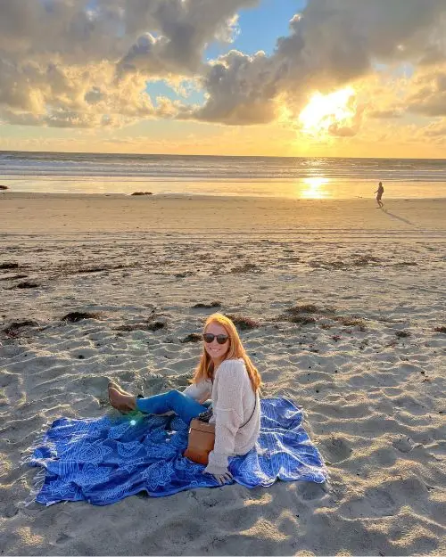 Lauren Kessel sitting on a wide open beach during sunset on a blanket