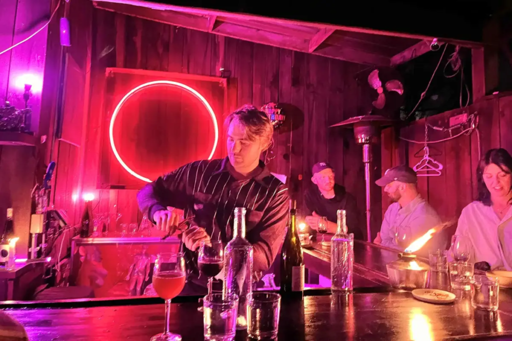 Bartender pouring a drink in front of a circular neon pink sign, which shows how cool of a bar Pink Moon Bar Asheville is