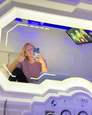 Woman sitting in the Izzzleep pod taking a photo in the mirror to show the size