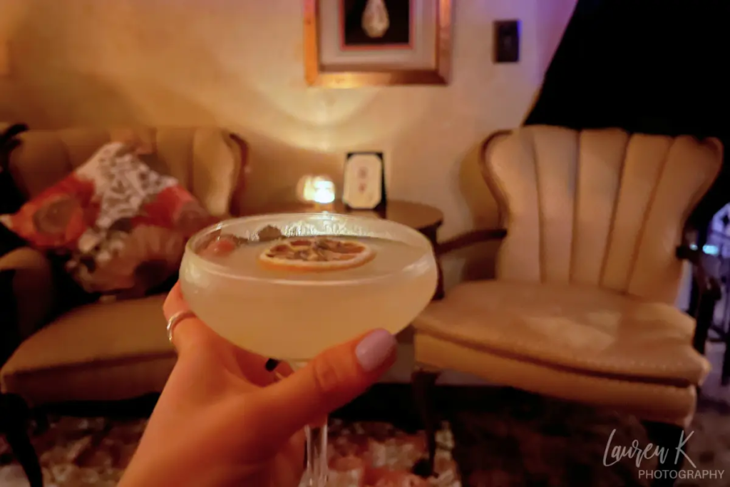 Cover image for the Charleston SC speakeasy blog which shows a cocktail held out in a dimly lit room with antique furniture