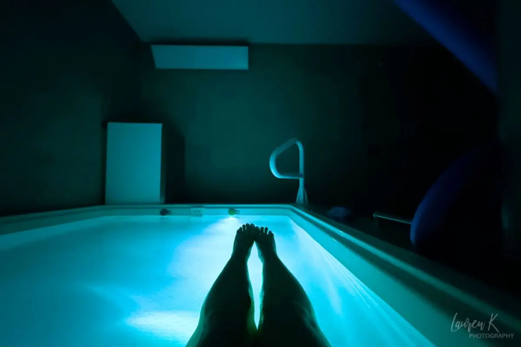 Cover image for the Synergy Float Center review which shows a person's legs floating in a float tub lit up with blue lights