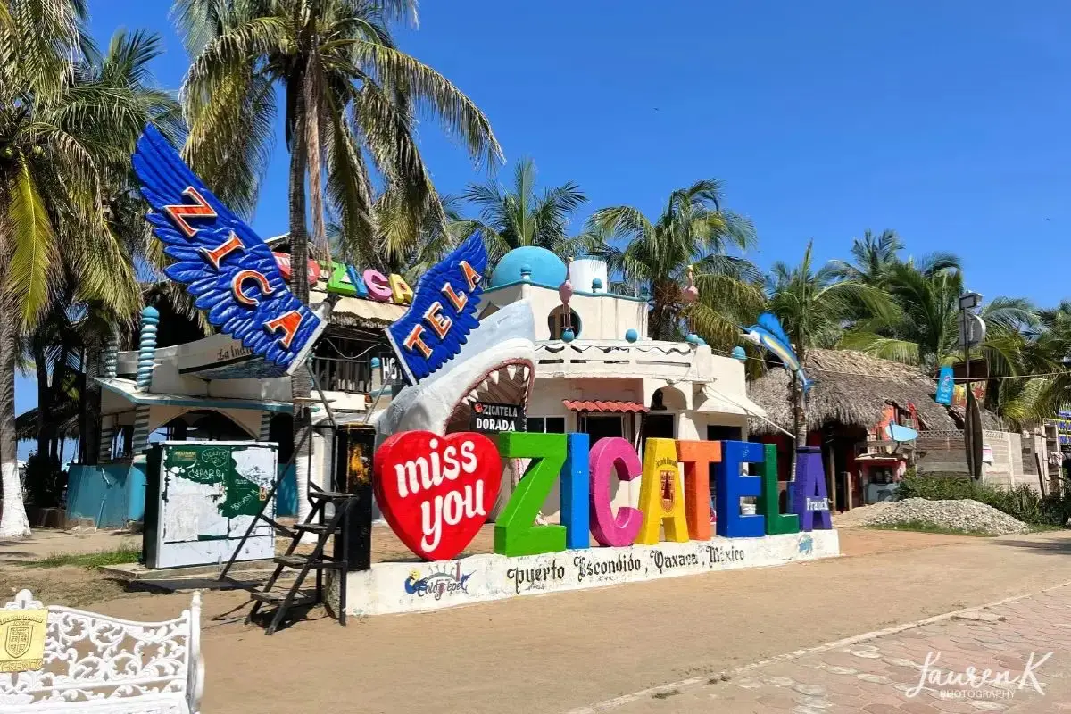 The Zicatela sign on the beach in Puerto Escondido, with palm trees behind and truly looking like a tropical paradise, to display one of the areas for where to stay in Puerto Escondido on vacation